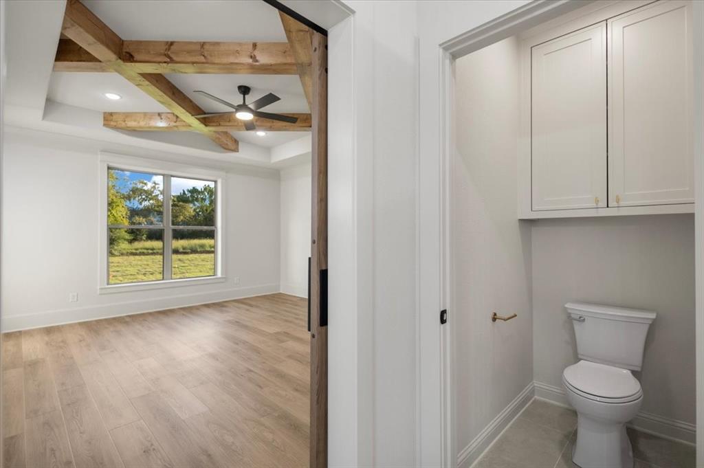 Tray ceiling with wood beam accents, wood-finish flooring, ceiling fan, and a large window