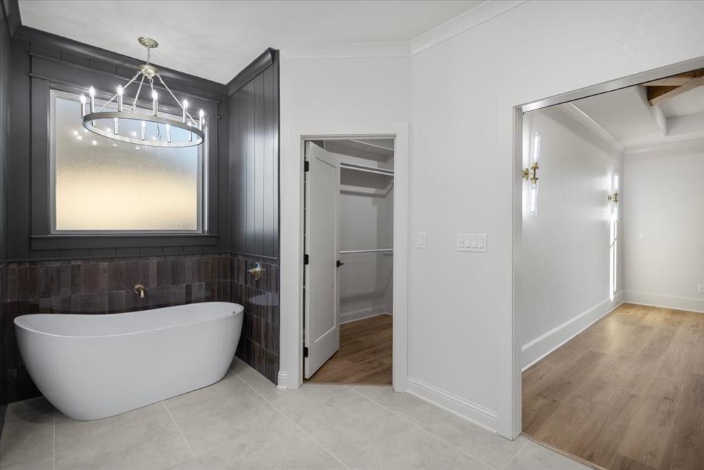 Freestanding bathtub with a bronze-finish faucet, dark wood wall paneling, and a contemporary chandelier
