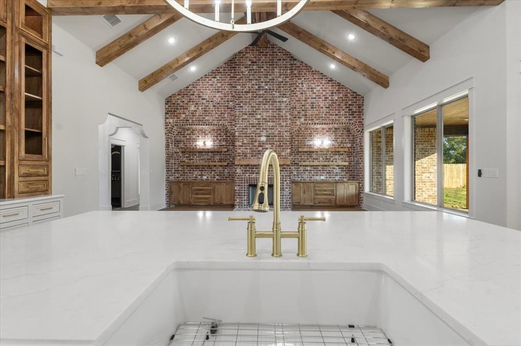 White farmhouse sink with a gold-finish faucet, white countertop, and exposed wood ceiling beams