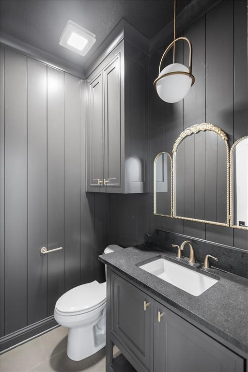Board and batten wall paneling, built-in cabinetry, dark stone countertop, undermount sink, and decorative lighting fixture