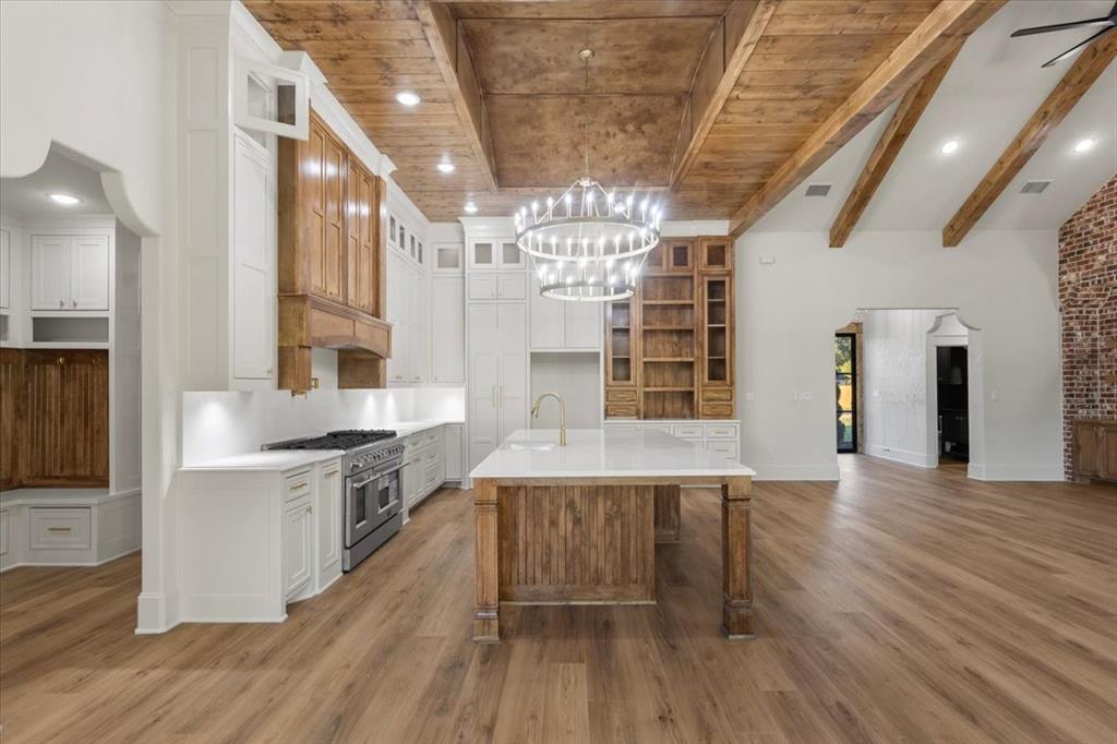 Gourmet kitchen with white cabinetry, wood-finish flooring, a large central island, stainless steel range, and a decorative chandelier