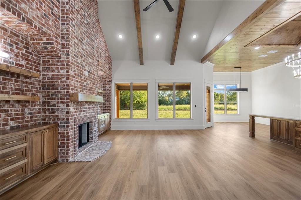Soaring vaulted ceiling with exposed wood beams, brick fireplace with wood mantle, wood-finish flooring, recessed lighting, and large windows