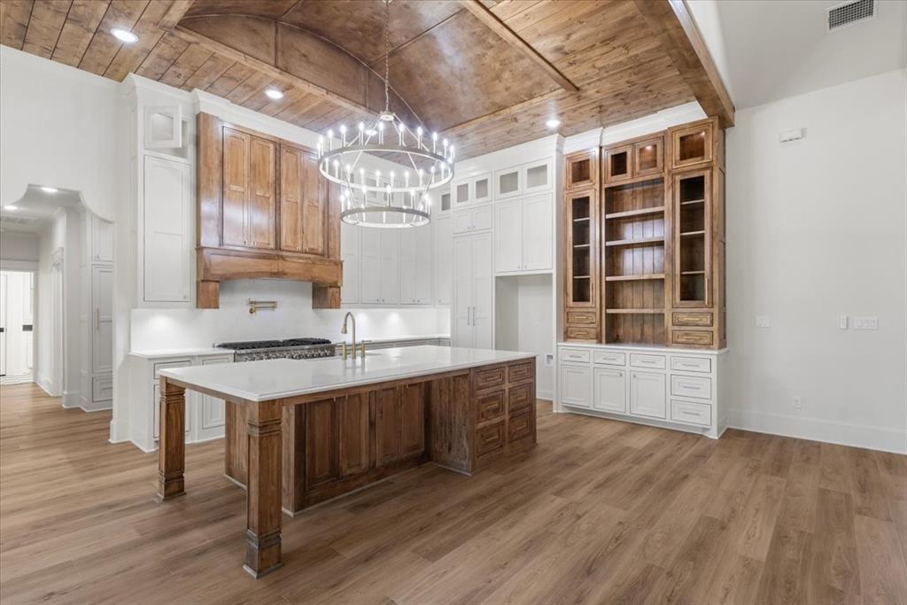Vaulted wood-paneled ceiling with recessed lighting, large kitchen island with a light-toned countertop, wood-finish flooring, wood cabinetry, and a built-in shelving unit