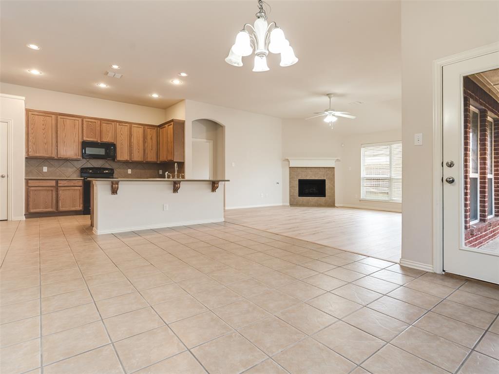 Open-concept area featuring tile flooring, a kitchen with wood cabinetry and a breakfast bar, recessed lighting, and a brick-surround fireplace