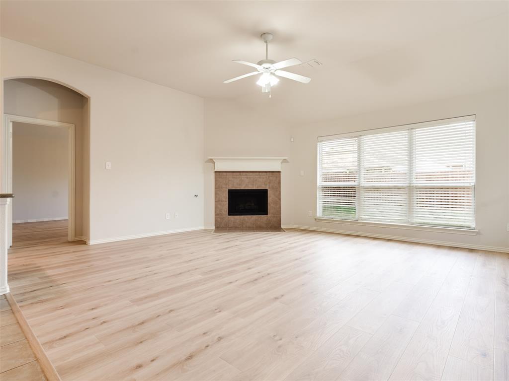 Living area featuring wood-finish flooring, a corner fireplace with tile surround, vaulted ceilings with a ceiling fan, and large windows with horizontal blinds