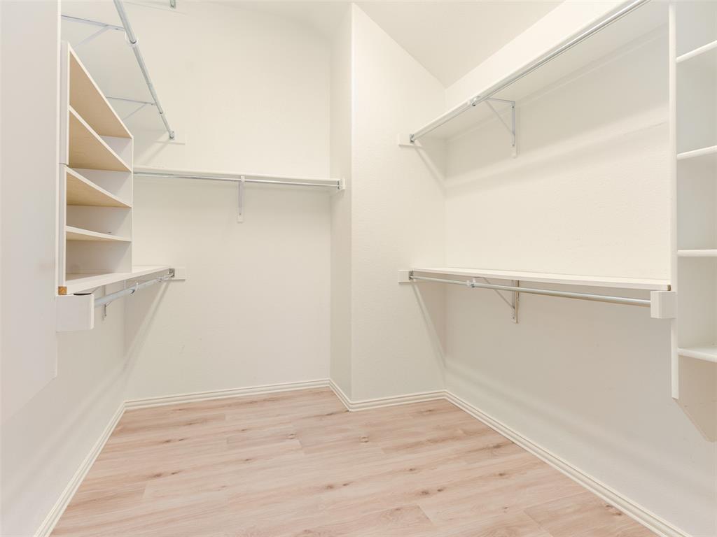 Walk-in closet featuring light wood-finish flooring and extensive built-in shelving units with integrated hanging rods