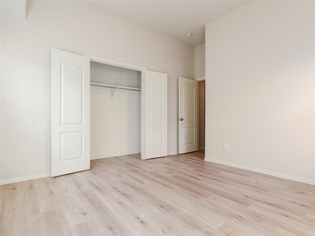 Room featuring wood-finish flooring, neutral walls, two-panel interior doors, and a reach-in closet with built-in shelving