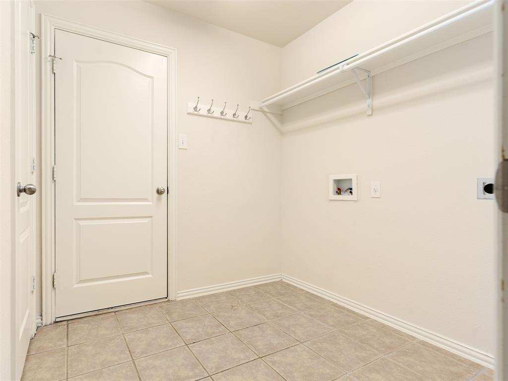 Neutral-toned tile flooring, white paneled door with hardware, wall-mounted storage rack, and fixed shelving