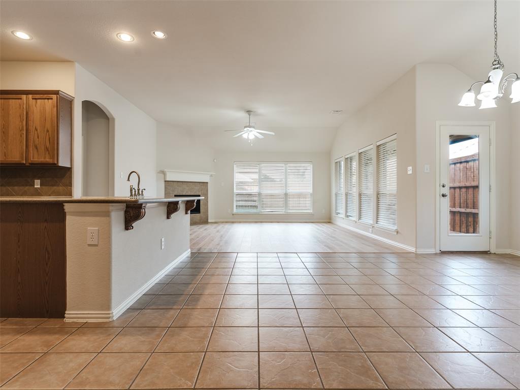 Open-concept space featuring tile flooring, wood-finish cabinetry, a peninsula with a stone countertop, a fireplace with a mantel, and wood-finish flooring