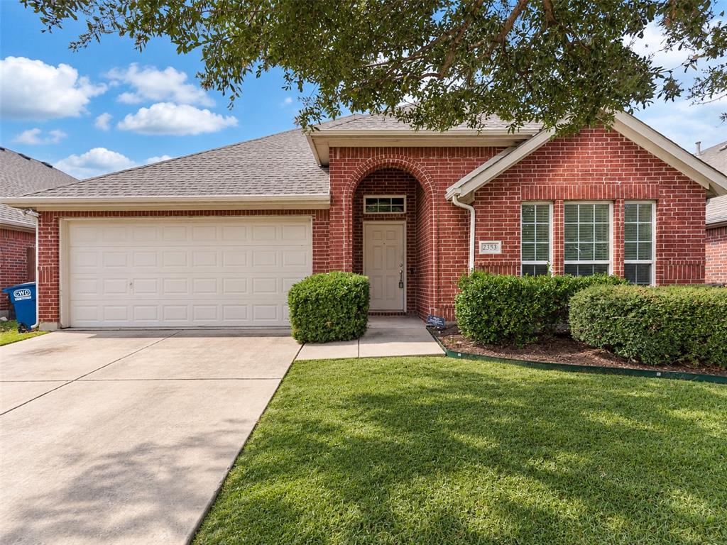 Red brick exterior featuring an arched entryway, a double-car garage, and a concrete driveway