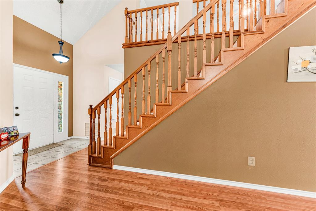 A grand, open-foyer entryway features soaring high ceilings, tiled floors, and a dramatic wooden staircase that creates an impressive first impression. It offers an inviting space to welcome friends and family as they step inside your home.