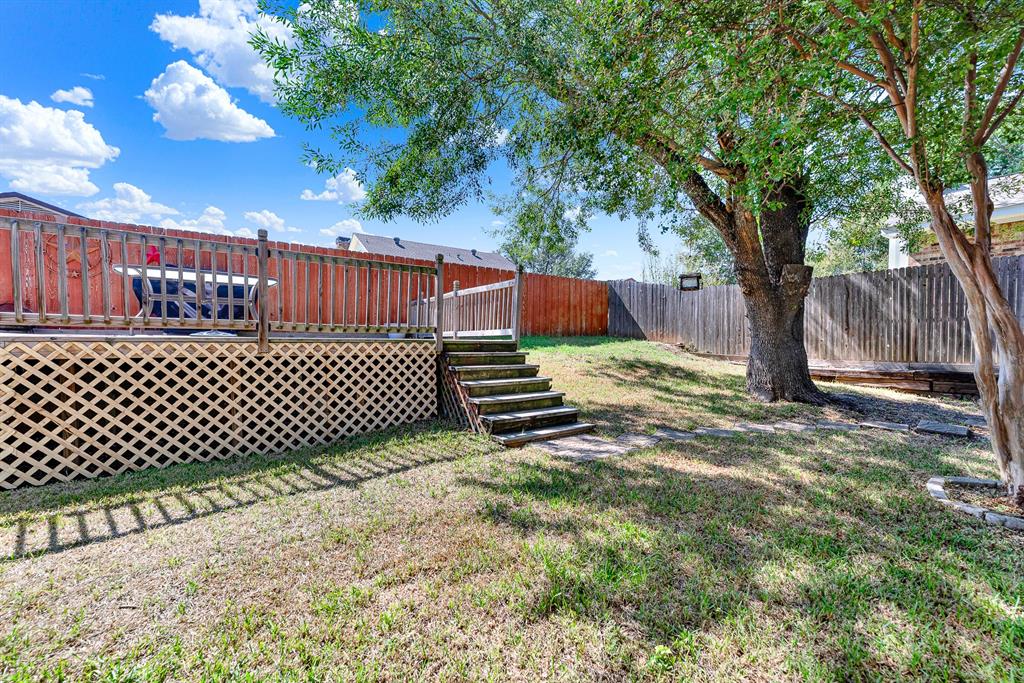 Stepping stones lead past mature trees toward the elevated deck stairs in a quiet, fully fenced yard. It is a wonderful setting for outdoor pets to play freely while you soak in the fresh air