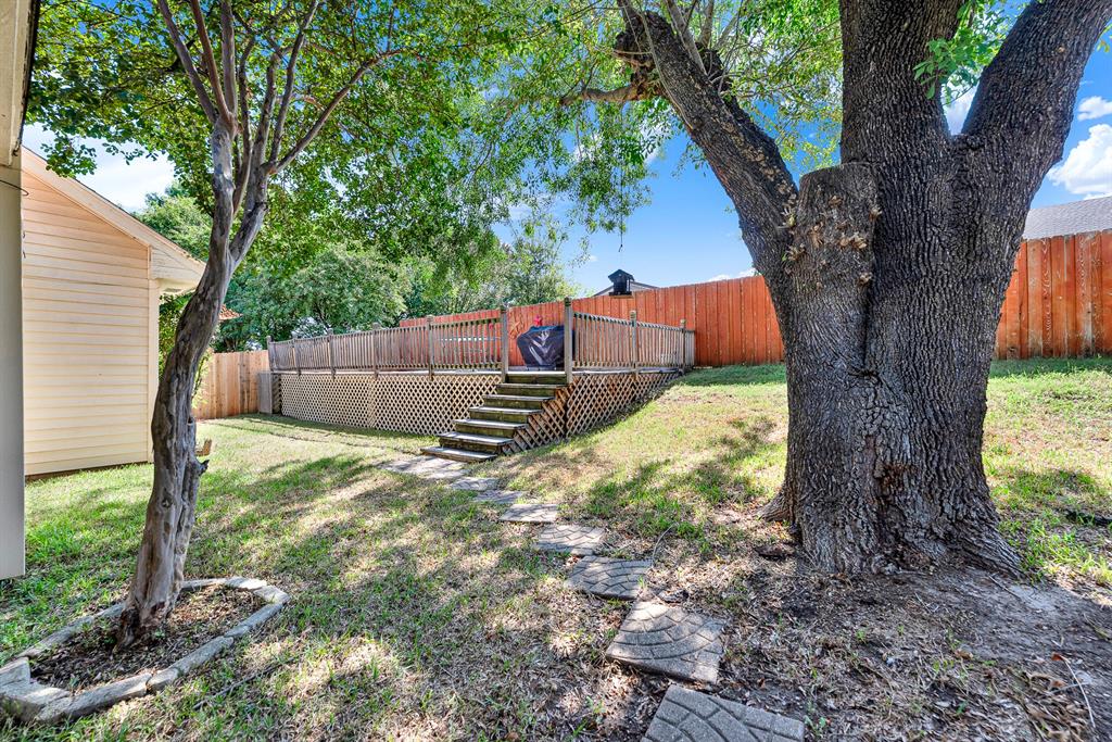 A grand shade tree towers over the grassy lawn, leading toward a raised wooden sun deck with lattice detailing. You will love spending sunlit afternoons enjoying the private backyard atmosphere