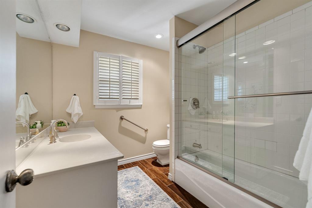 The guest bathroom is a great size and features wood like ceramic tile, a large vanity and a tub-shower combination with a sliding glass door and white tile surround.