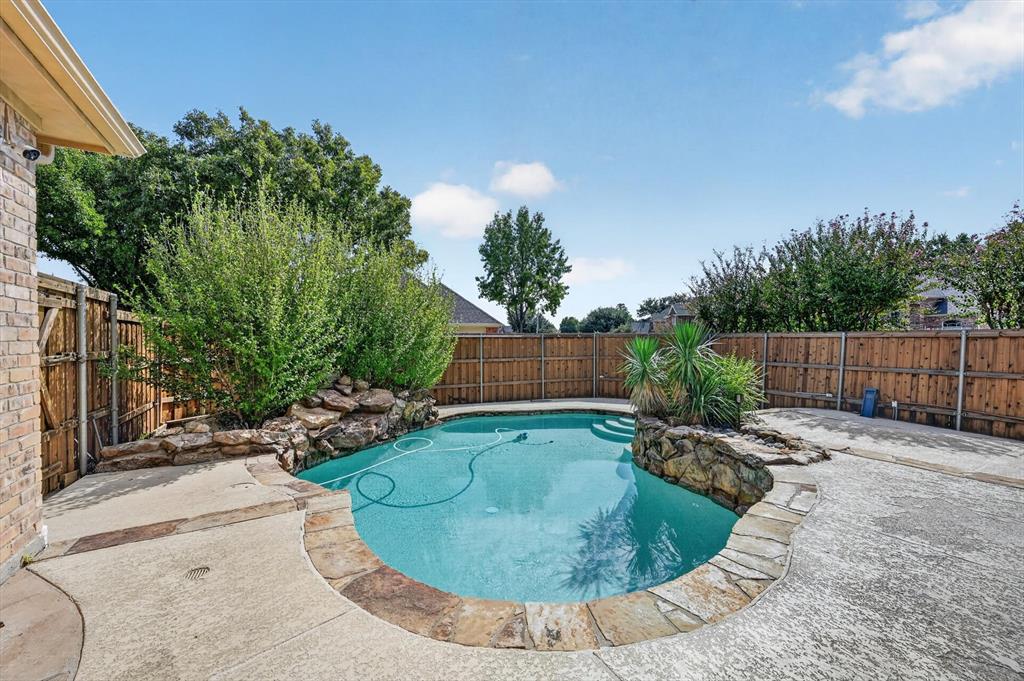 In-ground swimming pool featuring stone accents, integrated rock landscaping, a stone coping perimeter, and surrounding concrete decking enclosed by wood fencing