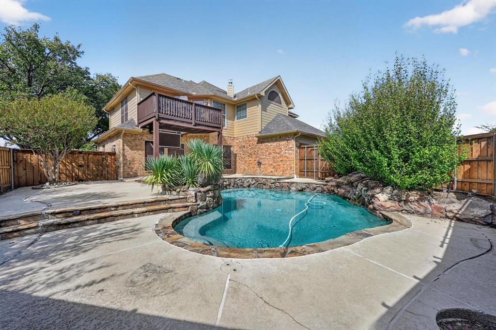 Exterior backyard featuring a stone-lined pool, elevated deck, multi-level concrete patio, and perimeter wood fencing