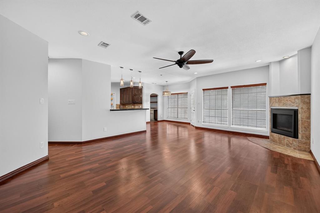 Living space featuring wood-finish flooring, a corner fireplace with stone surround, recessed lighting, a ceiling fan, and a kitchen breakfast bar with pendant lighting
