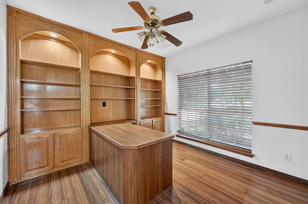 Built-in oak cabinetry with arched shelving, integrated lighting, wood-finish flooring, and a central workspace desk