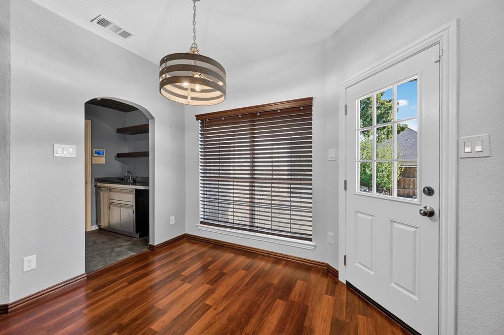 Wood-finish flooring, arched entryway, drum-style pendant light, and exterior door with glass panes