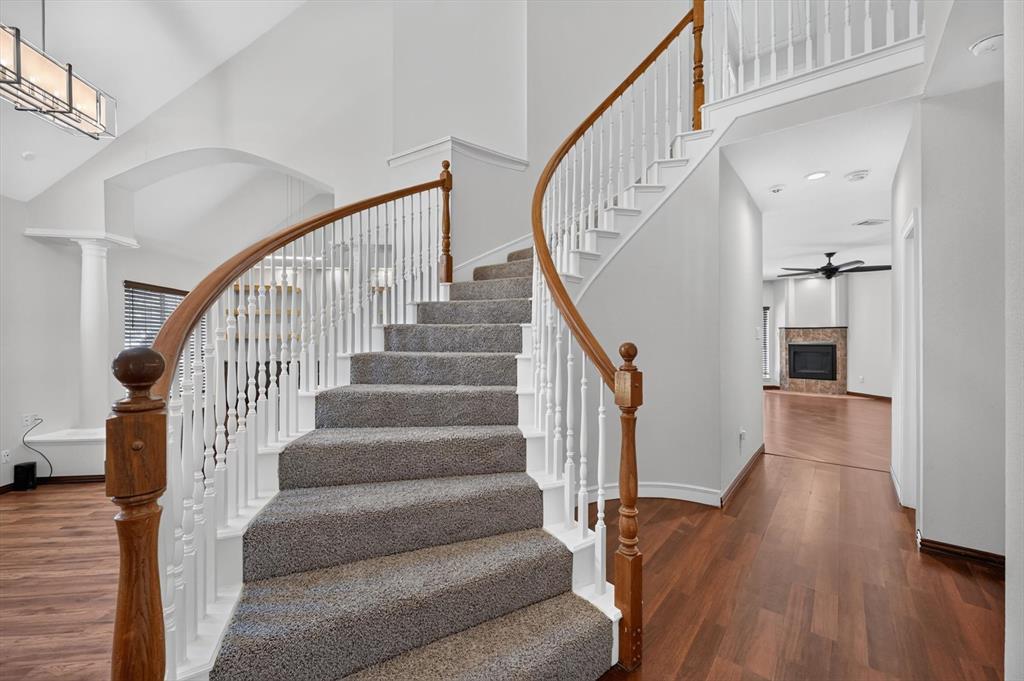 Curved staircase with wood handrails, white balusters, and carpeted treads, featuring a two-story ceiling, recessed lighting, and wood-finish flooring