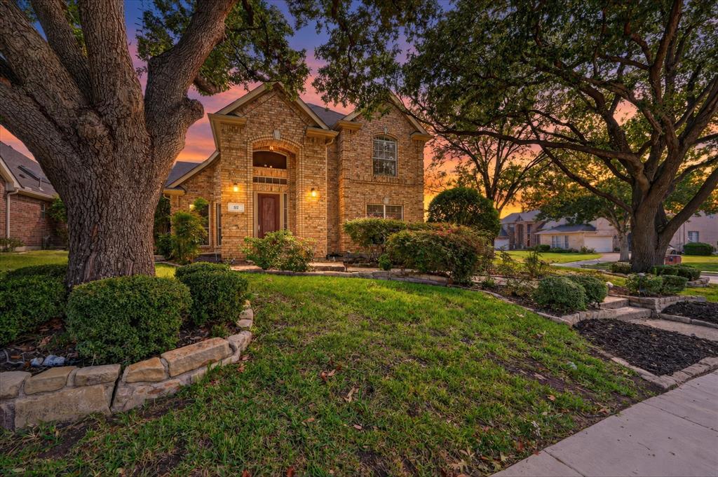 Brick exterior featuring an arched entryway, stone-bordered landscape beds, and mature shade trees