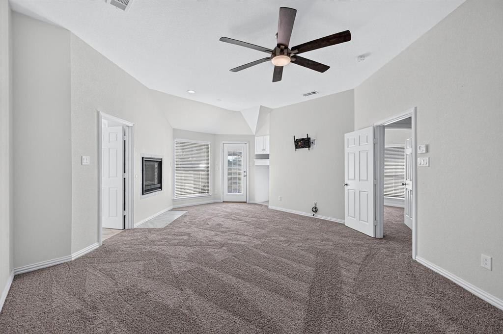 Vaulted ceiling featuring a central five-blade ceiling fan, wall-mounted gas fireplace, neutral wall-to-wall carpeting, and a glass-paneled exterior door
