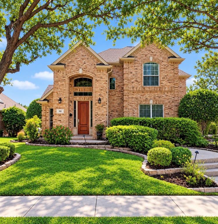 Two-story brick exterior featuring a prominent arched entryway, wood-panel door, stone-edged landscaping, and a multi-gabled roofline Two-story brick exterior featuring a prominent arched entryway, wood-panel door, stone-edged landscaping, and a multi-gabled roofline