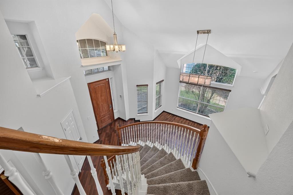 Curved staircase featuring a wooden handrail and white balusters, vaulted ceilings, arched windows, wood-finish flooring, and multi-light hanging fixtures