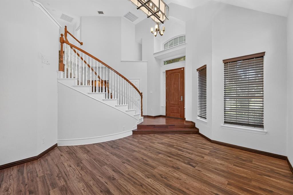 Foyer featuring vaulted ceilings, wood-finish flooring, a curved staircase with wooden handrail, arched transom window, and chandelier