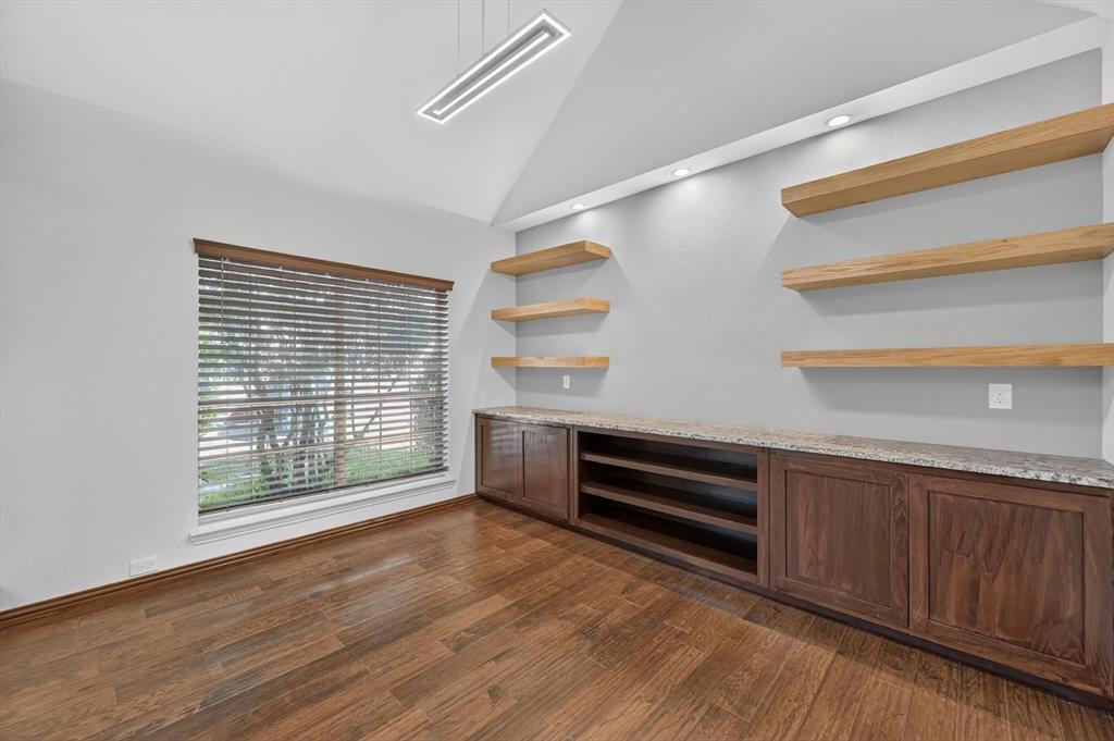 Vaulted ceiling, built-in cabinetry with stone-finish countertops, natural wood floating shelves, recessed lighting, and wood-finish flooring