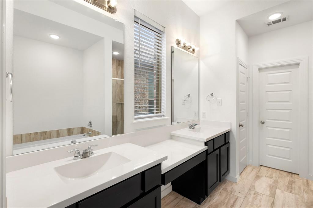 Dual vanity with dark cabinetry, light-toned composite countertops, large wall-mounted mirrors, and tile flooring