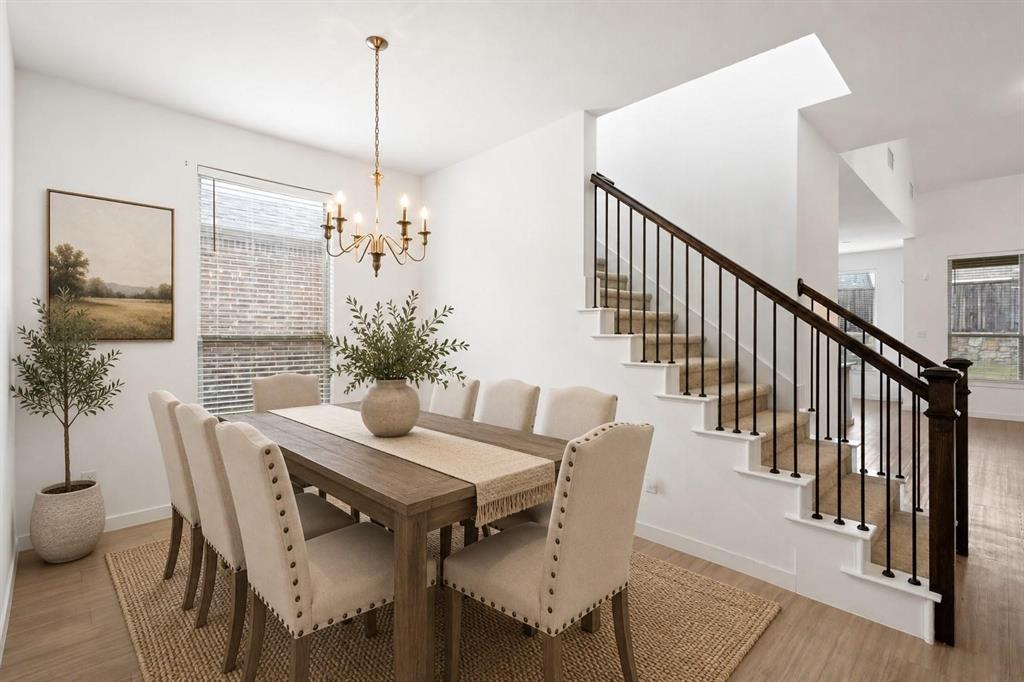 Open-concept interior featuring wood-finish flooring, a multi-arm chandelier, and a staircase with dark wood handrails and black metal balusters Open-concept interior featuring wood-finish flooring, a multi-arm chandelier, and a staircase with dark wood handrails and black metal balusters