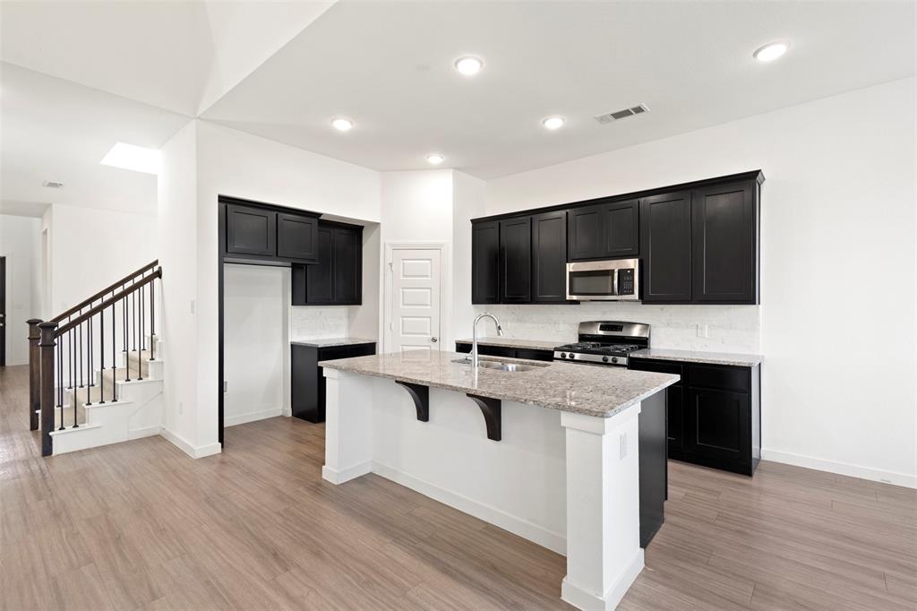 Kitchen featuring dark cabinetry, stone-finish countertops, a central island with a sink, recessed lighting, and wood-finish flooring