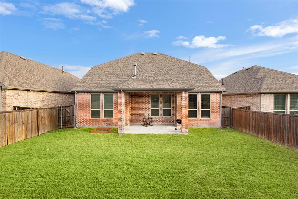 Full brick exterior with a covered rear patio, expansive grass lawn, and wood privacy fencing