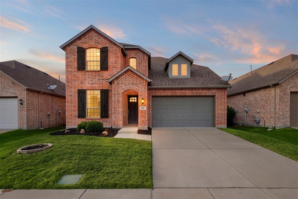 Two-story brick exterior featuring a shingled roof, decorative shutters, a covered arched entryway, and an attached two-car garage