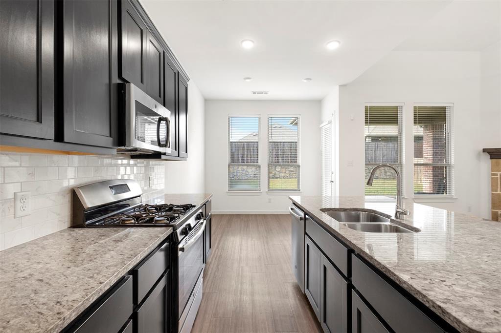 Kitchen featuring dark cabinetry, stone-finish countertops, stainless steel appliances, subway tile backsplash, and wood-finish flooring