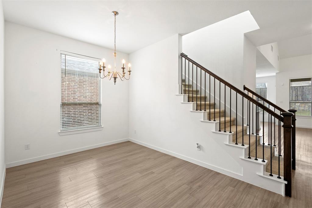 Open-concept space featuring wood-finish flooring, a traditional multi-arm chandelier, and a staircase with a dark wood handrail and black iron balusters
