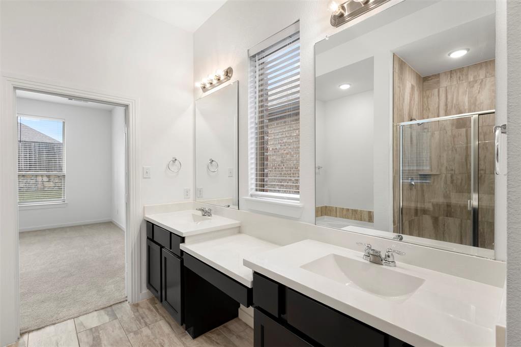 Dual-sink vanity with dark cabinetry and stone countertops, glass-enclosed shower featuring tiled surround, and large wall-mounted mirrors