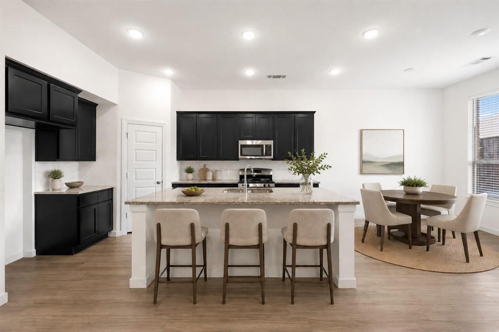 Kitchen featuring black cabinetry, a central island with a stone countertop, recessed lighting, and wood-finish flooring Kitchen featuring black cabinetry, a central island with a stone countertop, recessed lighting, and wood-finish flooring