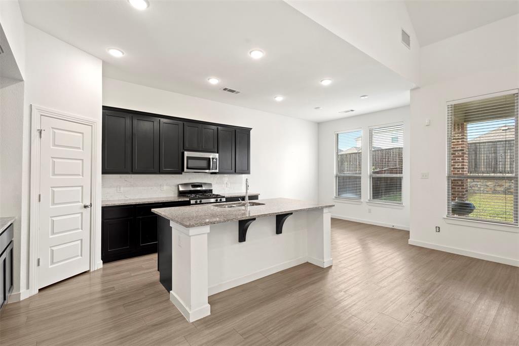 Kitchen featuring black cabinetry, stone-surface countertops, central island, wood-finish flooring, and vaulted ceilings