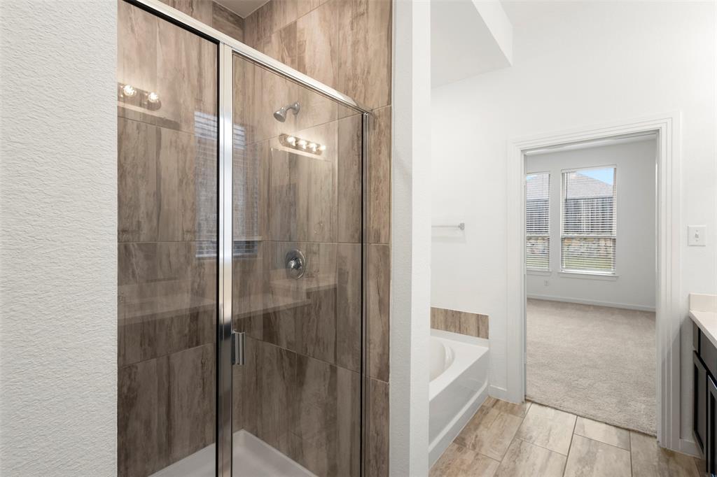 Walk-in shower with wood-patterned tile surround, glass enclosure, chrome shower fixture, soaking tub, and tile flooring