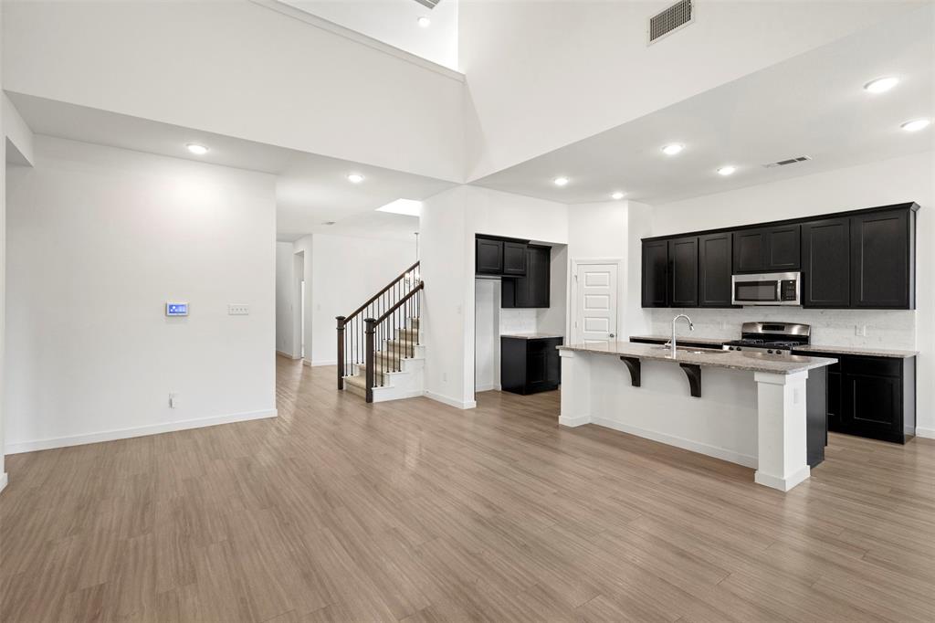 Open-concept kitchen featuring dark cabinetry, stone-finish countertops, a center island, vaulted ceilings, and wood-finish flooring