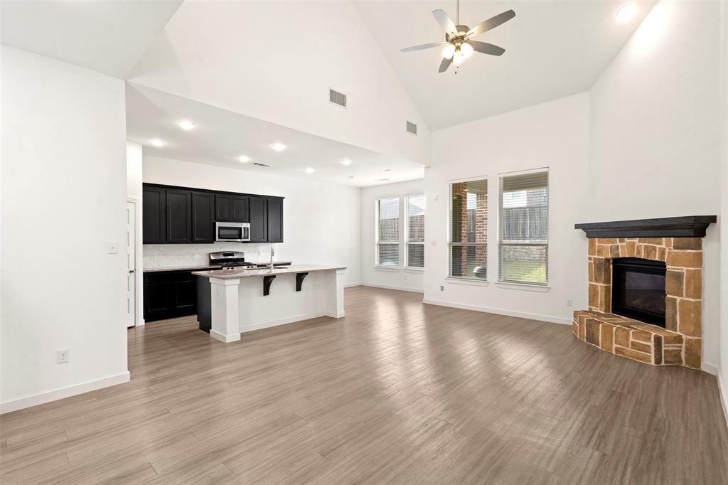 Vaulted ceilings featuring recessed lighting, a stone-surround fireplace with a wooden mantel, wood-finish flooring, and a kitchen equipped with dark cabinetry and a central island