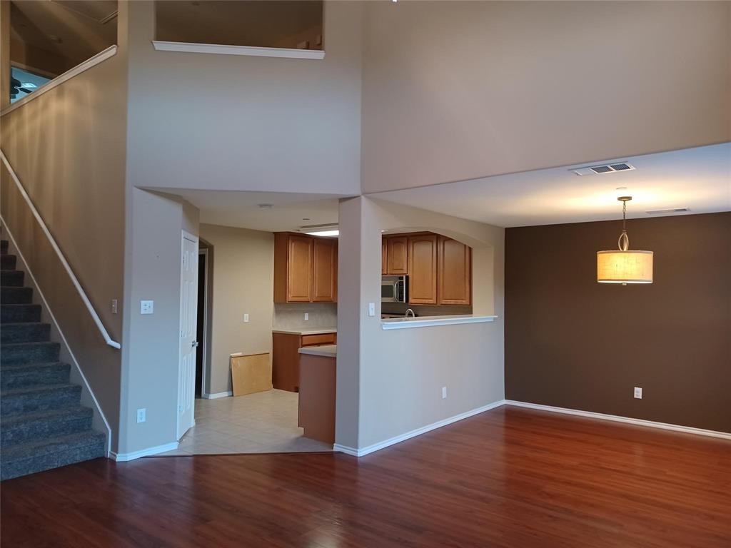 High ceilings, wood-finish flooring, staircase with carpeted treads, kitchen pass-through, and a decorative pendant light fixture