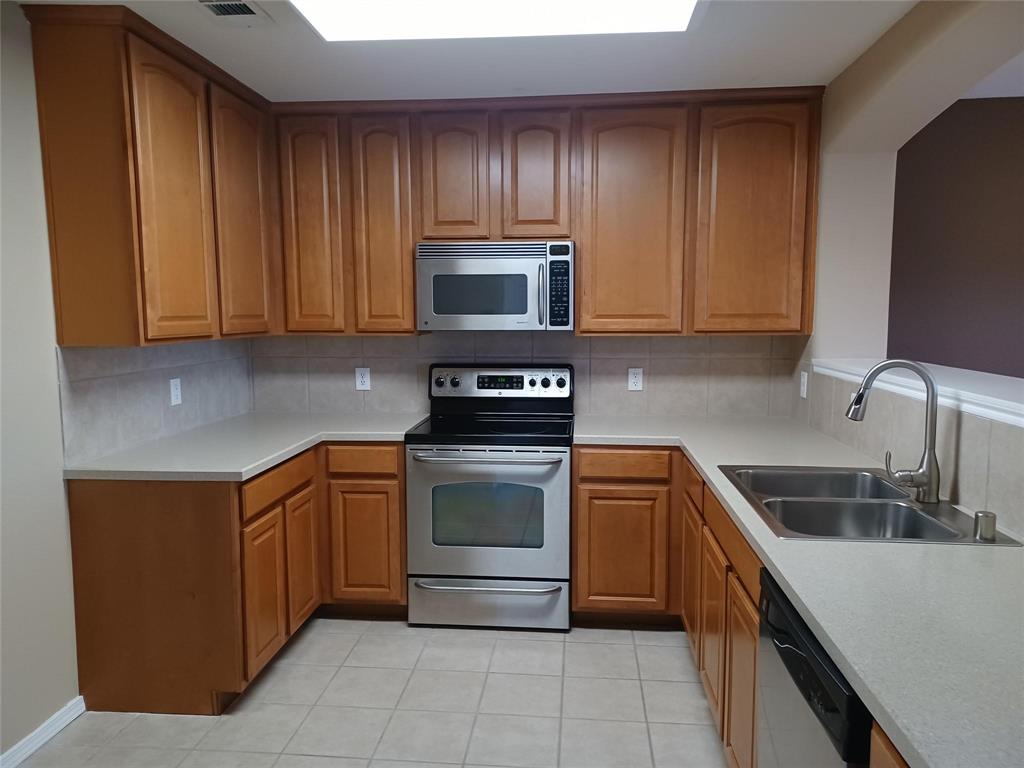 U-shaped kitchen featuring wood cabinetry, stainless steel appliances, light-toned countertops, tile backsplash, and tile flooring
