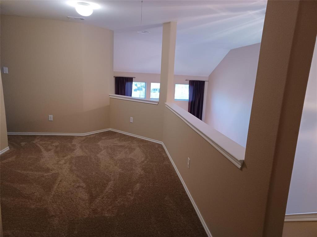 Carpeted loft area with a partial wall overlooking a lower space and vaulted ceilings
