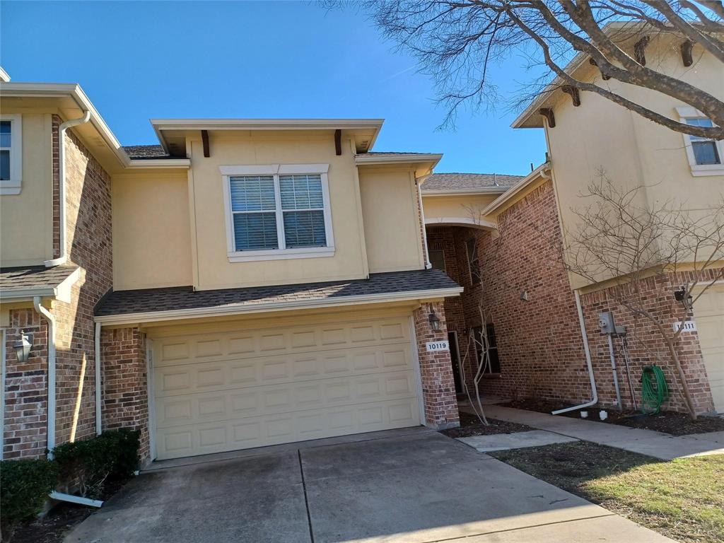 Stucco and brick exterior with a two-car garage, upper-level window with blinds, and decorative eave brackets