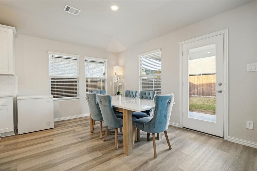 Neutral-toned interior space featuring wood-finish flooring, three double-pane windows with horizontal blinds, and a full-glass panel door
