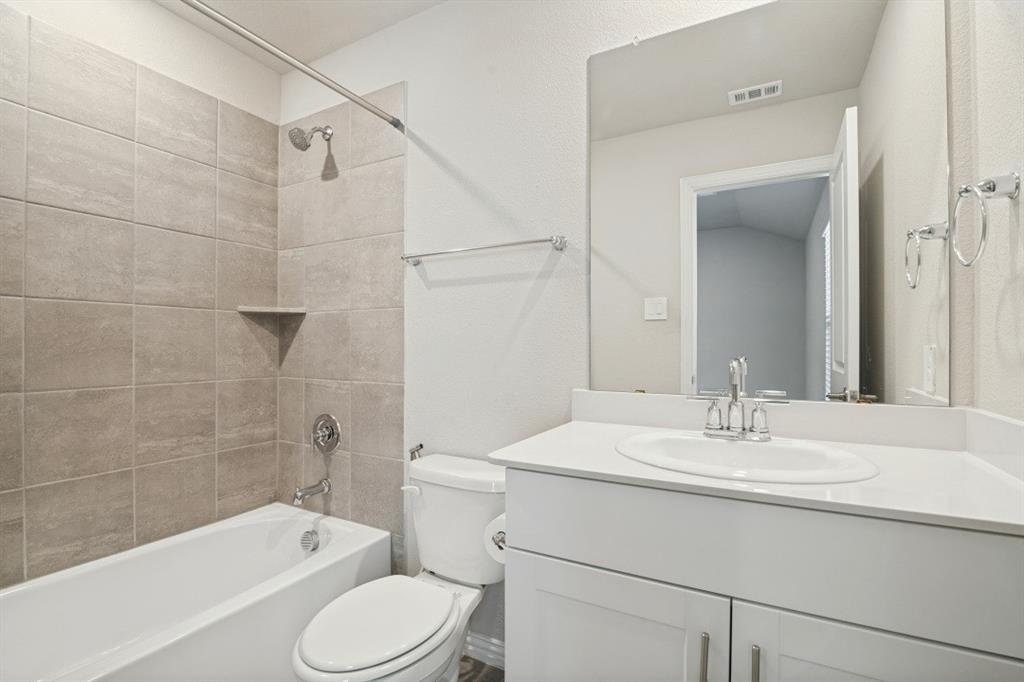 Bathroom featuring a white vanity with a composite countertop and integrated sink, a large wall-mounted mirror, and a tub-shower combination with floor-to-ceiling textured tile surrounds