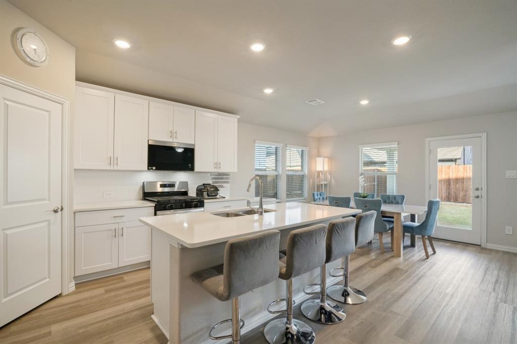 Kitchen featuring white cabinetry, an expansive central island with a solid-surface countertop, integrated undermount sink, recessed lighting, and wood-finish flooring